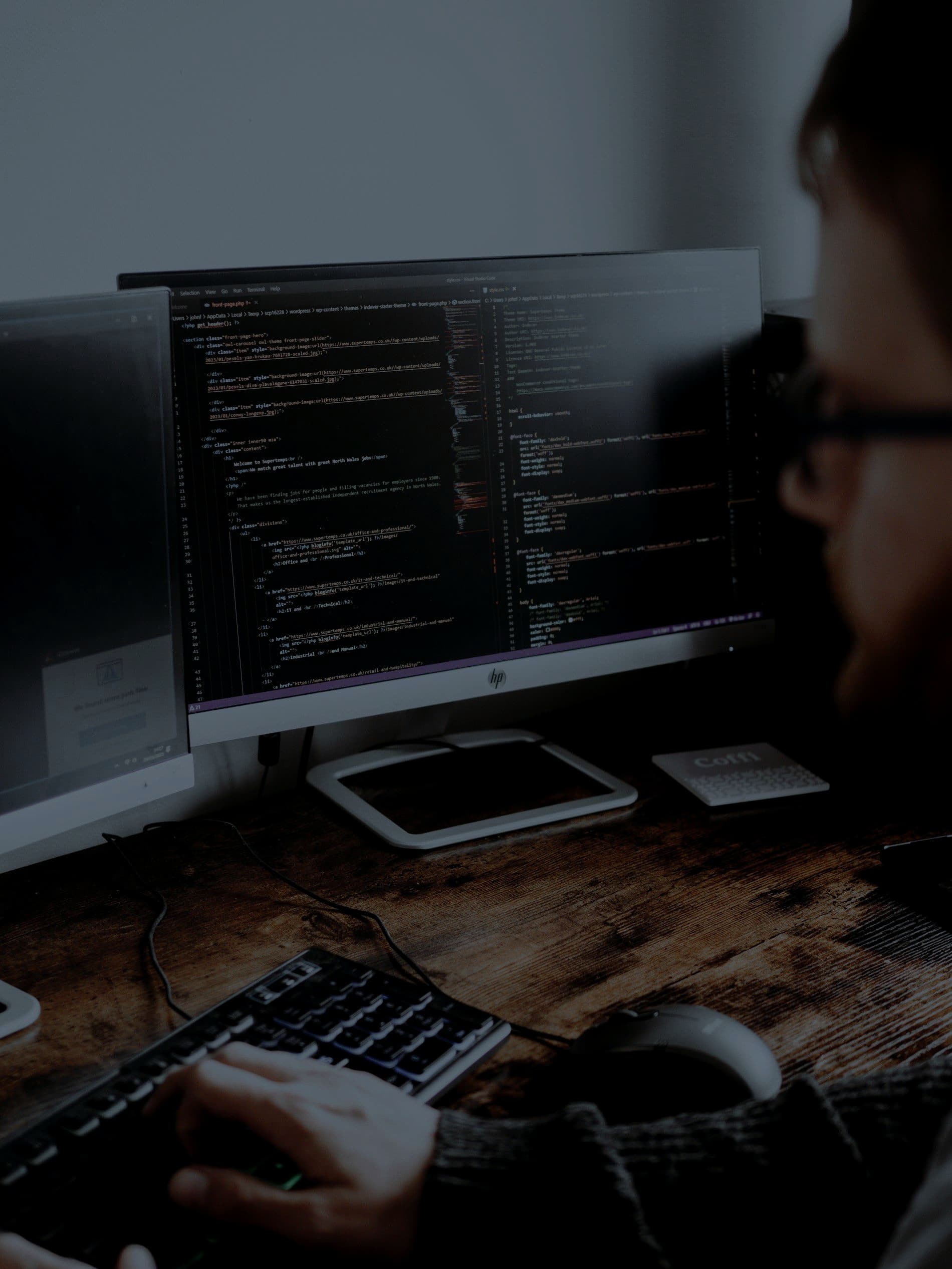 A software engineer working at monitors full of code in a dim room