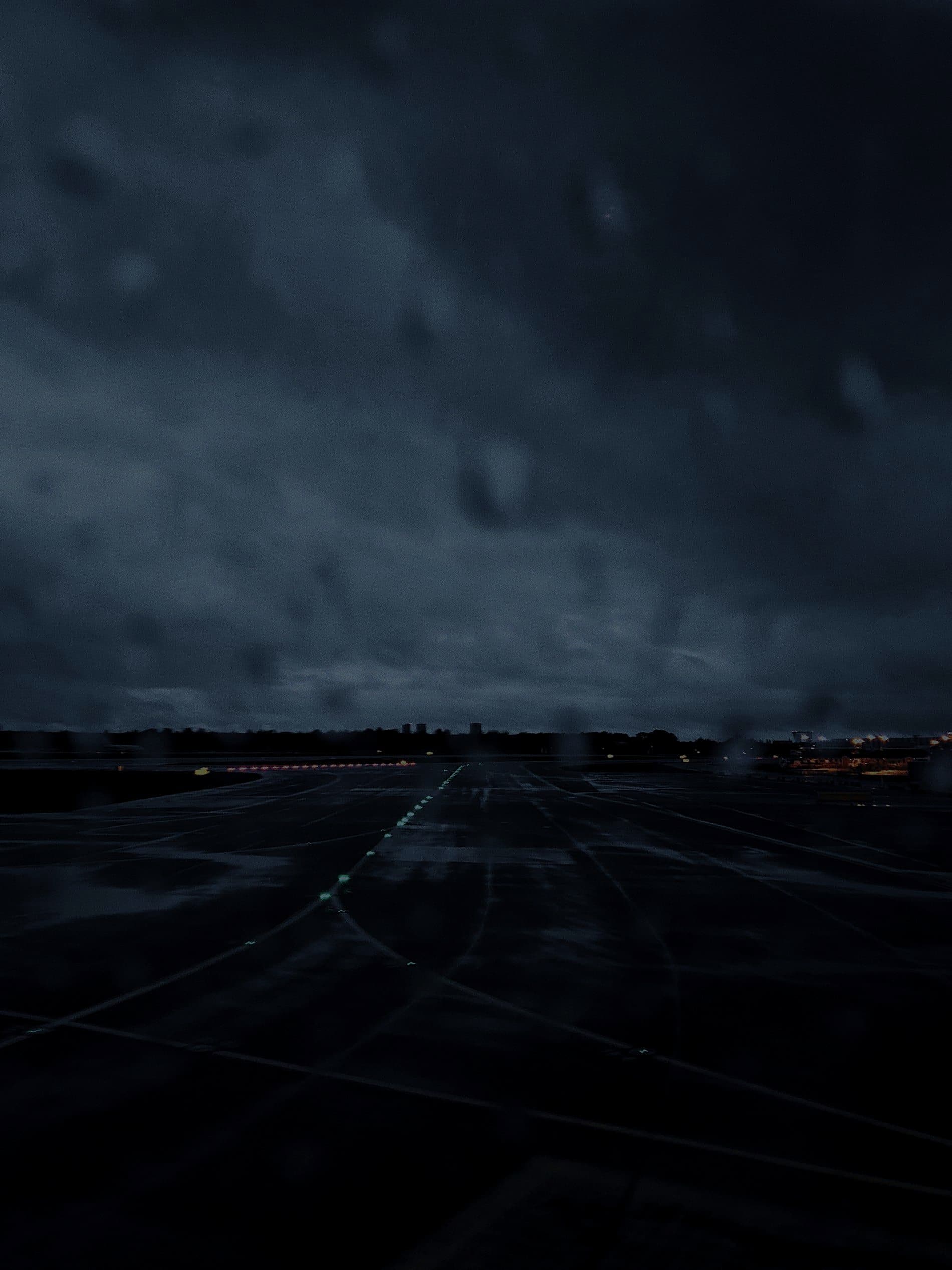 A wet runway and apron lights under storm clouds
