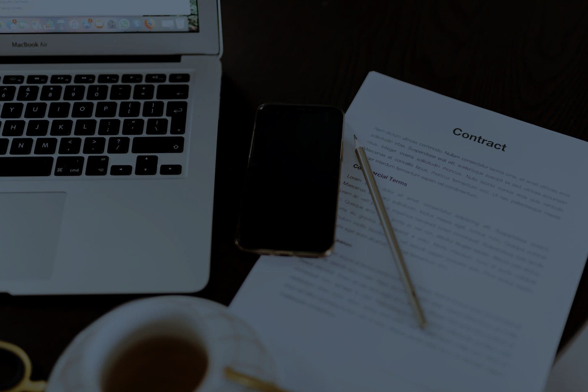 A laptop, phone and contract document on a desk